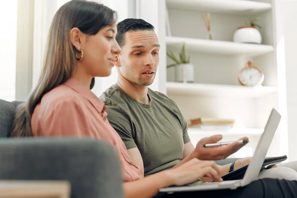discusión en casa y pareja con portátil en el sofá para información y decisión sobre reserva de viajes online hombre mujer y relax con tecnología en el salón para plan de viaje registro web y lectura de reseñas