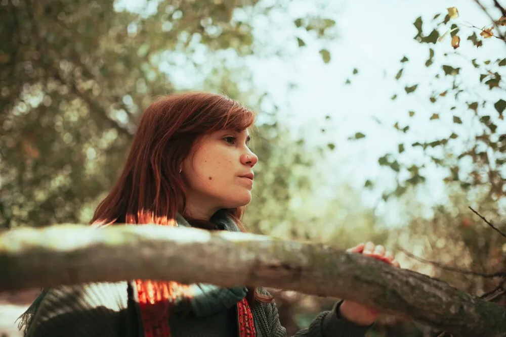 Contrapicado de una mujer joven mirando hacia otro lado en el bosque