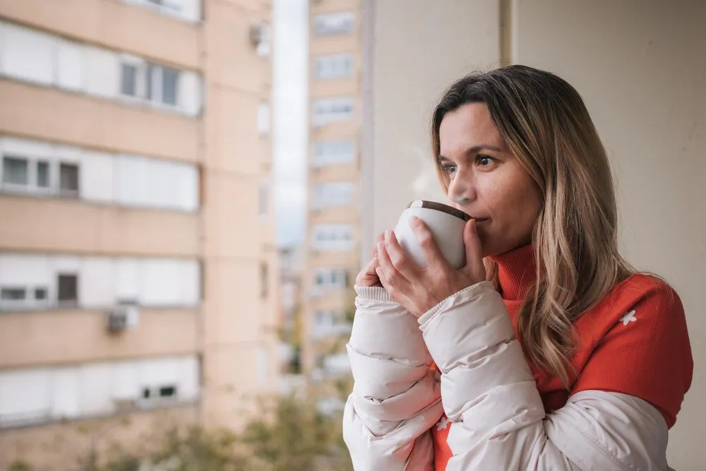 Mujer hermosa bebiendo café caliente en la terraza preparándose para un nuevo y frío día de invierno.