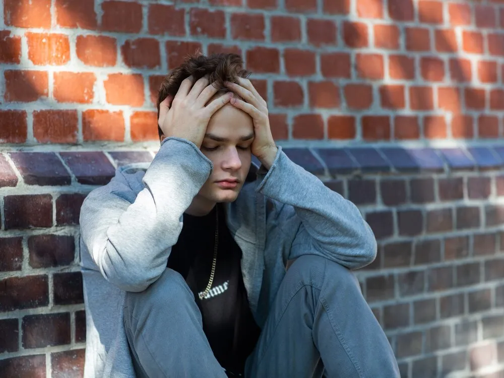 Retrato de un adolescente triste y solitario con una sudadera con capucha en la calle, problemas y psicología de los adolescentes, concepto. Joven sujetándose la cabeza.