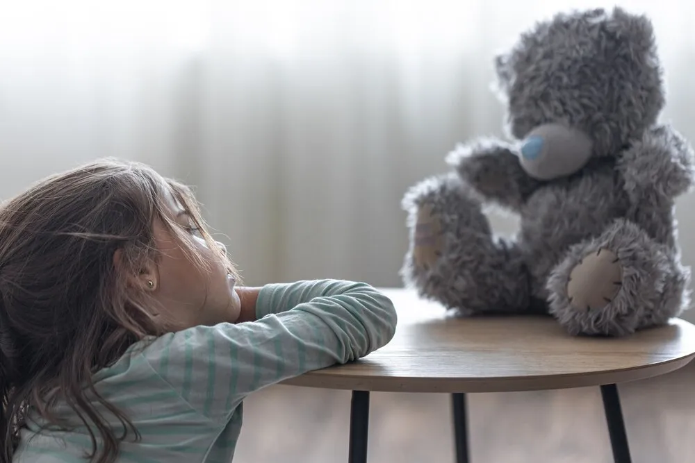 una niña pequeña mira a su osito de peluche, una niña con su juguete favorito sobre un fondo desenfocado con espacio para texto.