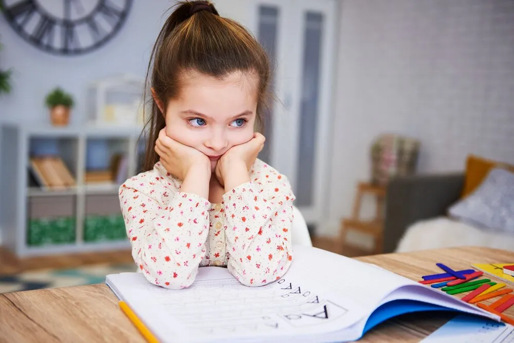niña aburrida y triste haciendo los deberes en casa
