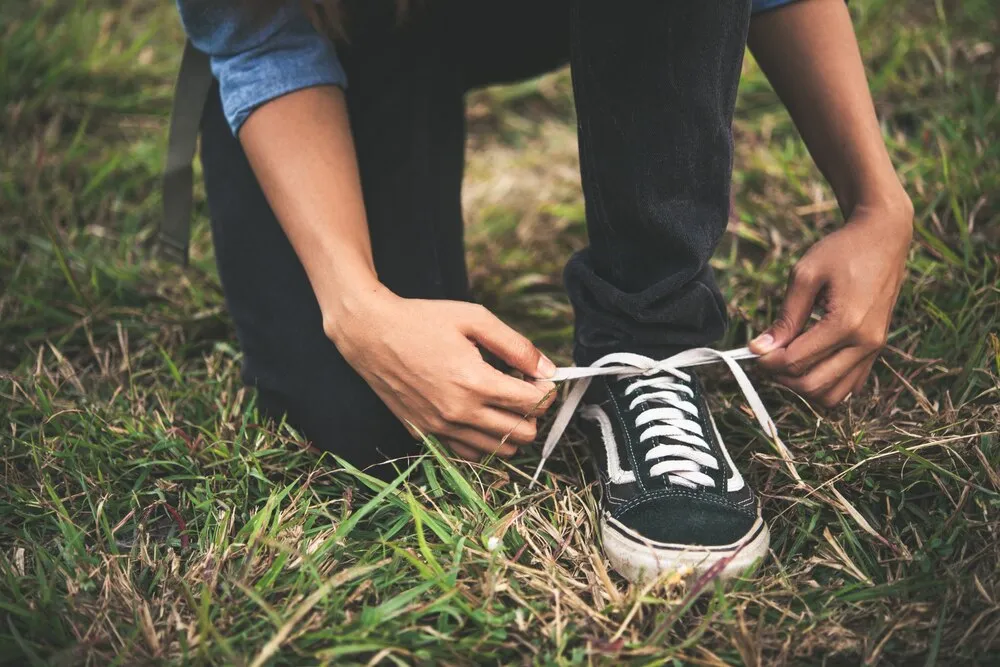 Joven mochilera atándose los cordones mientras hace senderismo por el bosque.