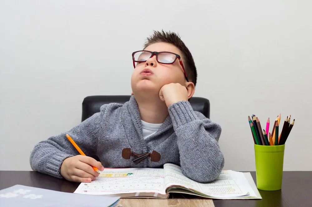 niño frustrado con los deberes, escribiendo en casa. niño estudiando en la mesa. niño dibujando con un lápiz.