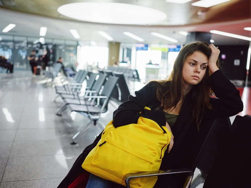 mujer con expresión facial triste esperando en el aeropuerto mochila amarilla