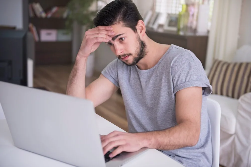 joven cansado trabajando en casa con su ordenador portátil